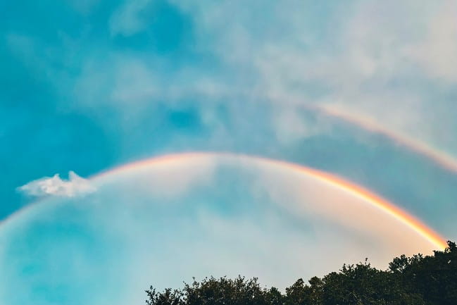 A double rainbow agains a partly cloudy sky.