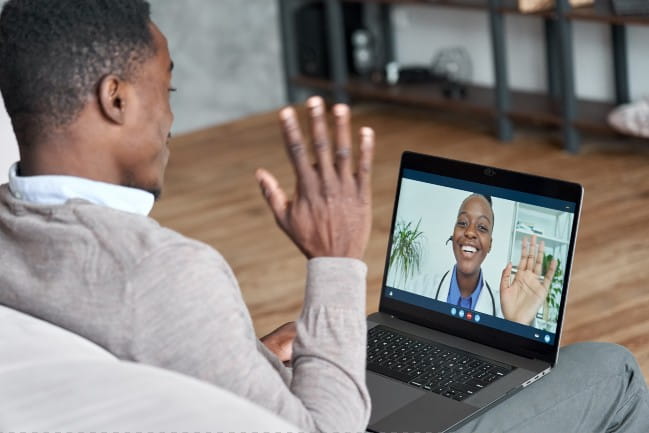 Man with laptop waving to provider on screen